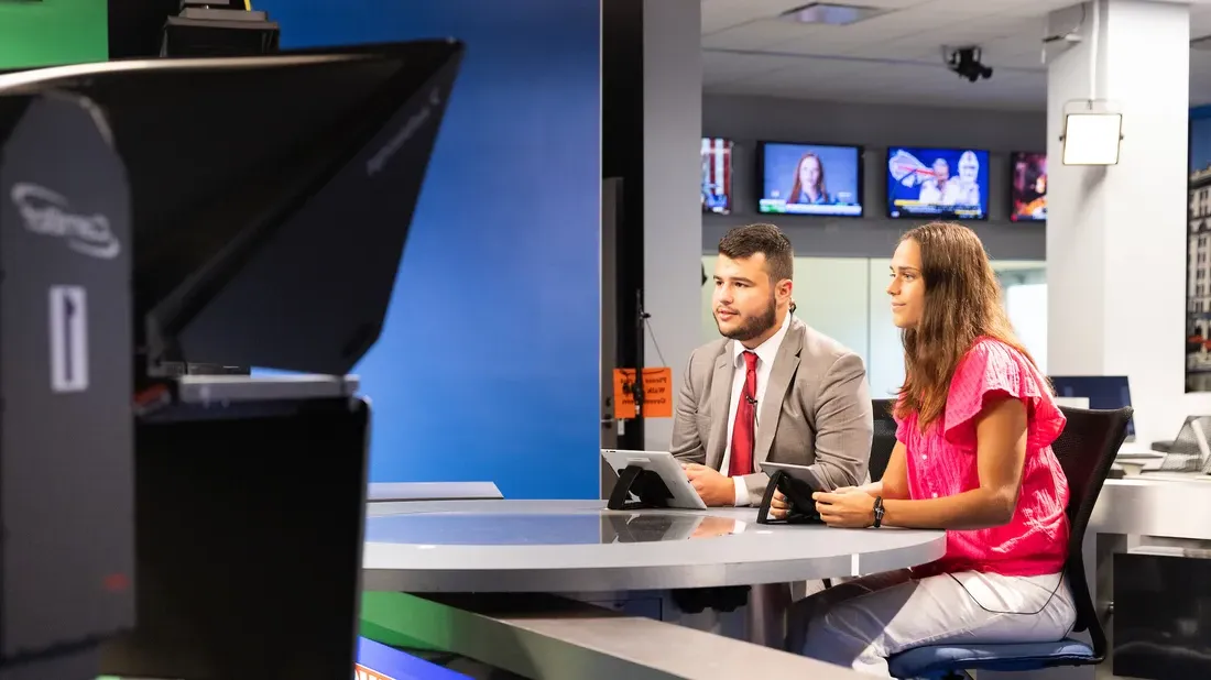 Students sitting at a television news desk.